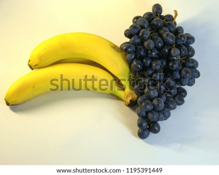 A bunch of ripe, tasty bananas, three pieces and a bunch of grapes. The picture was taken in the lightbox, close-up.
