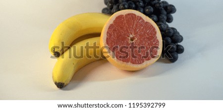 A bunch of ripe, tasty bananas, three pieces, a bunch of grapes and half a ripe grapefruit. The picture was taken in the lightbox, close-up.
