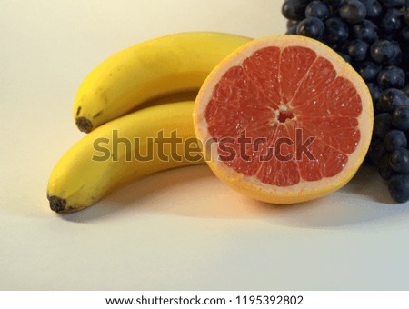 A bunch of ripe, tasty bananas, three pieces, a bunch of grapes and half a ripe grapefruit. The picture was taken in the lightbox, close-up.
