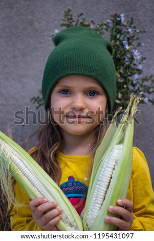 Young little baby girl holding with hands a bunch of raw white corn on the cob. Maize. Vegan vegetarian healthy food concept