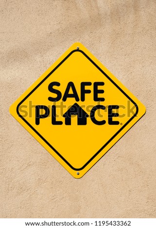 Yellow and Black Safe Place sign on a light adobe wall.