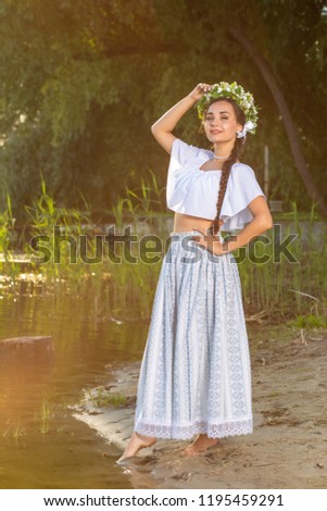 Young beautiful caucasian woman standing at the bank of river. Traditional countryside picture with girl at foreground and copy space.