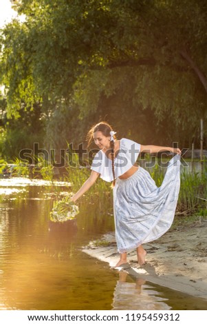 Young beautiful caucasian woman standing at the bank of river. Traditional countryside picture with girl at foreground and copy space. Sun flare