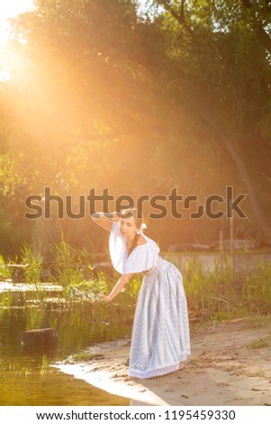 Young beautiful caucasian woman standing at the bank of river. Traditional countryside picture with girl at foreground and copy space. Sun flare