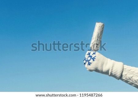 Female hand in knitted gloves with chocolate ice cream on the stick in the winter snowfall background. Concept