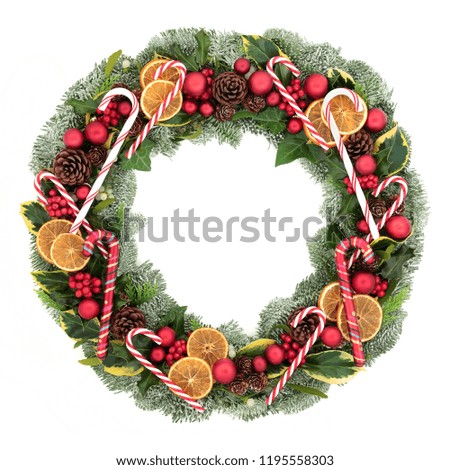 Festive Christmas and winter wreath with candy canes, bauble decorations, dried fruit, holly, mistletoe, ivy, pine cones and spruce fir isolated on white background.  