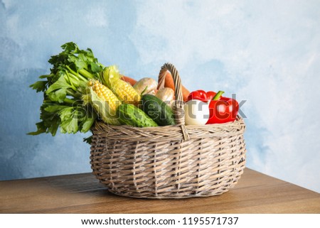 Basket full of fresh healthy vegetables on table against color background