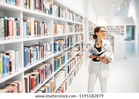 Young businesswoman searching books standing near the bookshelves at the modern white library