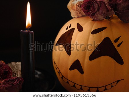 Halloween scary pumpkin face with rose herbarium and candle light on dark background