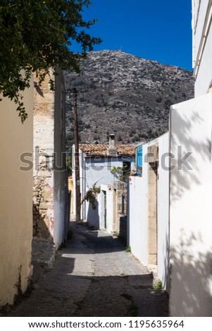 Narrow weathered road and pavement. Mostly white facades  of the houses. Blue sky. High rocky mountain in the background. Traditional village Archanes in the mountains  Crete, Greece.