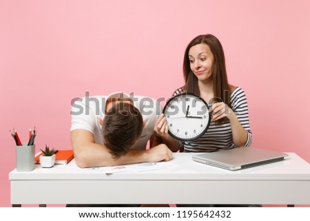 Two young fun shocked business woman man colleagues sit work at white desk with clock, laptop isolated on pastel pink background. Achievement career concept. Copy space advertising, youth co working