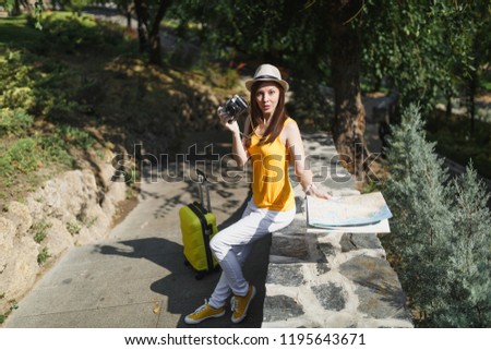Concerned traveler tourist woman in yellow clothes hat with suitcase city map holding retro vintage photo camera outdoor. Girl traveling abroad to travel on weekend getaway. Tourism journey lifestyle