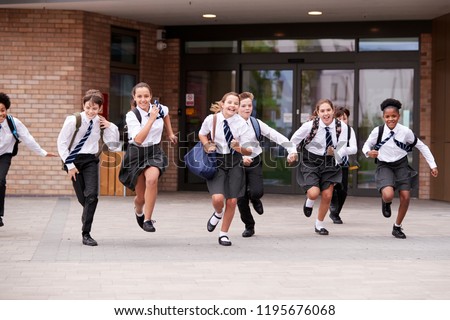 Group Of High School Students Wearing Uniform Running Out Of School Buildings Towards Camera At The End Of Class Royalty-Free Stock Photo #1195676068