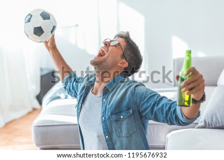 Excited mature man cheering while watching soccer match on sofa at home. Attractive, happy guy watching football, celebrating victory of his favorite team, yelling, having beer .