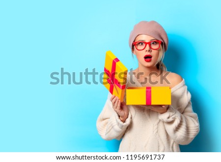 Portrait of a young girl in white sweater with yellow gift box on blue background