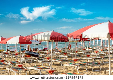 red and white umbrellas and sunlongers on the sandy beach in Italy Royalty-Free Stock Photo #119569195