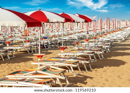 red and white umbrellas and sunlongers on the sandy beach in Italy Royalty-Free Stock Photo #119569210