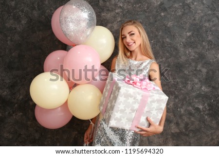 Beautiful young woman with gift box and air balloons on dark background