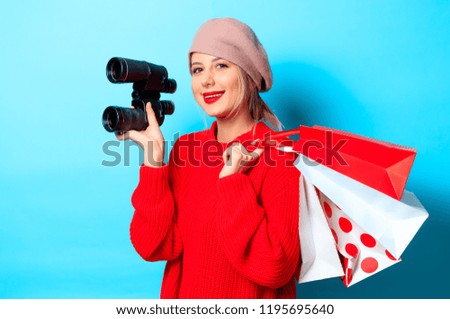 Portrait of a young girl in red sweater with bonocular box and shopping bag on blue background