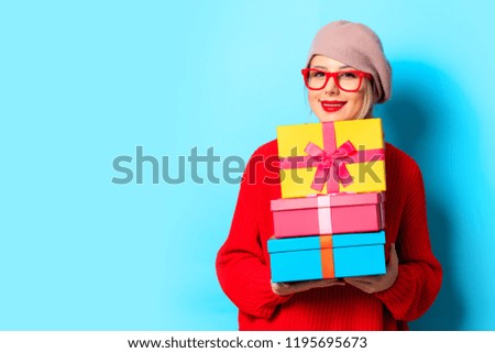 Portrait of a young girl in red sweater with gift boxes on blue background