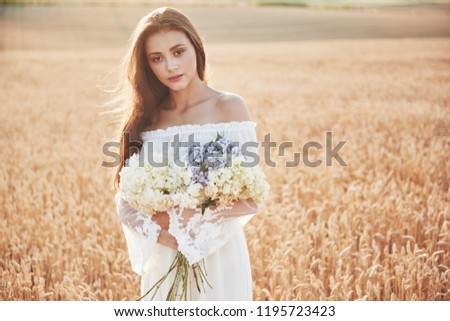 Beautiful girl in white dress running on the autumn field of wheat at sunset time