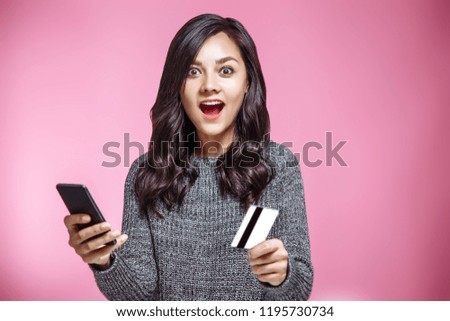 Portrait of a satisfied casual girl holding mobile phone and showing credit card isolated over pink background.