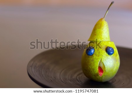 Funny green pear face with googly eyes and sticking out his tongue on a black wooden plate. The concept of Halloween.
