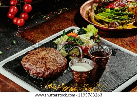 grilled meat patty with salad and two sauces (mayonnaise and ketchup) on a black plate on a copper background. close-up