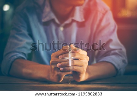 Closeup picture of a young Christian. He clasped hands and prayed God to bless the crucifix pendant, the symbol of the crucified Jesus by faith in Christ within the Catholic Church with copy space.