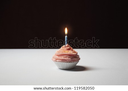 Pink baked cupcake with lighted candle on table isolated over black background