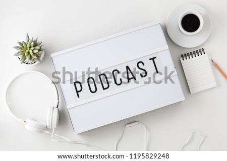 Podcast word on lightbox with headphones on white table, flat lay