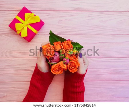 female hand holds gift box with bow, rose flower on pink wooden background