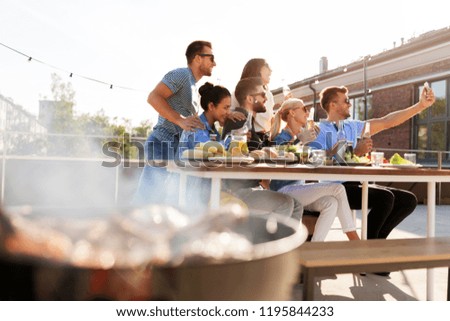 leisure and people concept - happy friends with drinks having barbecue party on rooftop in summer and taking selfie by smartphone