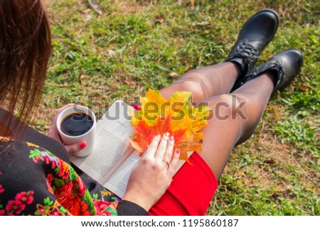 A girl drinks coffee and reads a book in nature