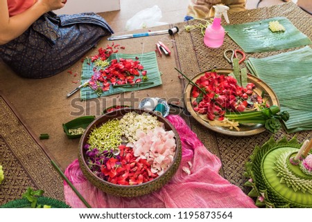 A asian woman stringing Thai tranditional jasmine garlands decorated with colorful flower petals