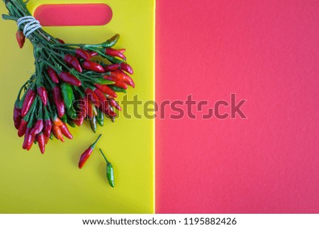 Red and green small pepper on tne yellow cutting board on the red background.Top view.Copy space.
