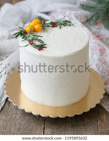 White New Year or Christmas cake, decorated with kumquat, sprigs of rosemary and cranberries on a wooden table. Winter cake. A birthday cake for those born in winter. Copy space, selective focus