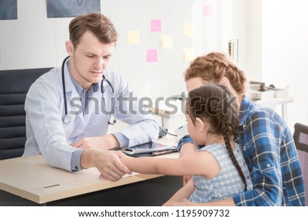 Pediatrician (doctor) man examining,reassuring and discussing child at surgery .Mother Caucasian and kid smiling in hospital room.Copy space.