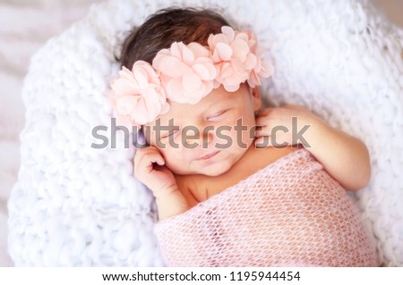 Cute and adorable newborn Caucasian girl smiling in her sleep. Pink head band with flowers and a light blanket, newborn photo session concept.
