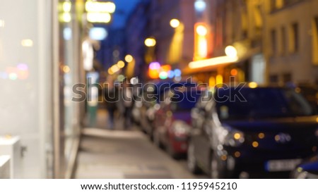 Out of focus background of cars parallel parked on city street next to shops