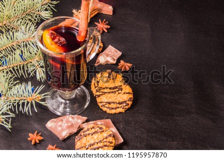 A glass of flavored mulled wine on a black leather background with biscuits pieces of chocolate chopsticks and a Christmas tree branch