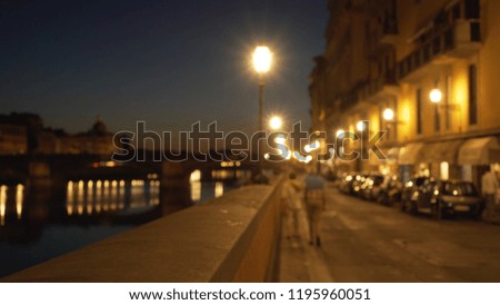 Blurry background of city street by Arno River at night in Florence, Italy