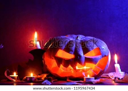 Halloween. Glowing pumpkin in dark blue light. Bat. Halloween pumpkin head jack lantern on wooden background. Autumn leaves and candles