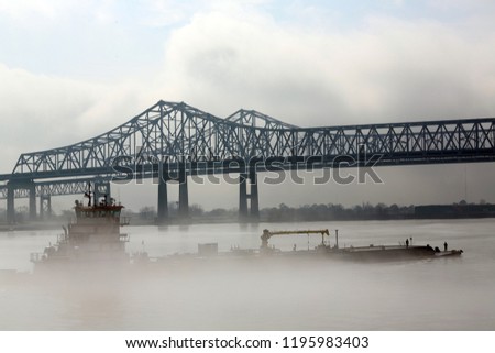 tug pushing barge on Mississippi River in fog with bridge in background, New Orleans, LA, USA