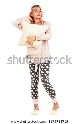 Young attractive smiling girl dressed in sleeping suit hugs the pillow and dreams about gifts. Christmas and New Year advertising concept. Studio shoot isolated on abstract blurred white background