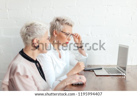 Two business women sitting at table in coffee shop, look at laptop. table laptop and cup of coffee