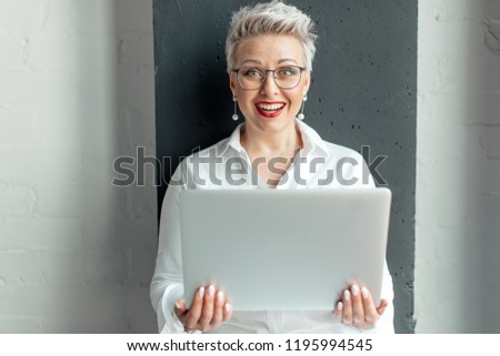 portrait of smile blonde business woman with laptop computer on grey wall background