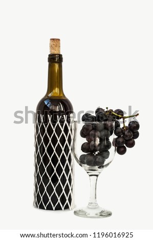 Glass goblet with grapes and a bottle of wine on a white background