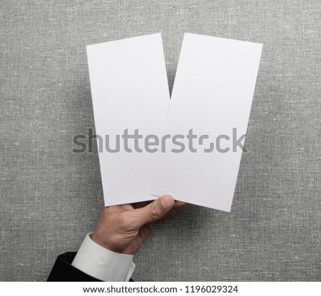 Mens hand holding empty white flyers on light gray background. Blank paper mock-up