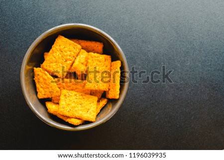 Top view of a dark brown dish filled with crackers on a black desk. Copy space for text.